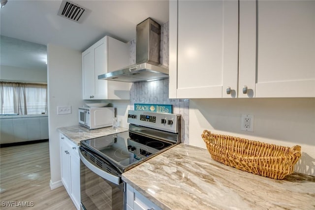 kitchen featuring white cabinets, stainless steel electric range, wall chimney range hood, and visible vents