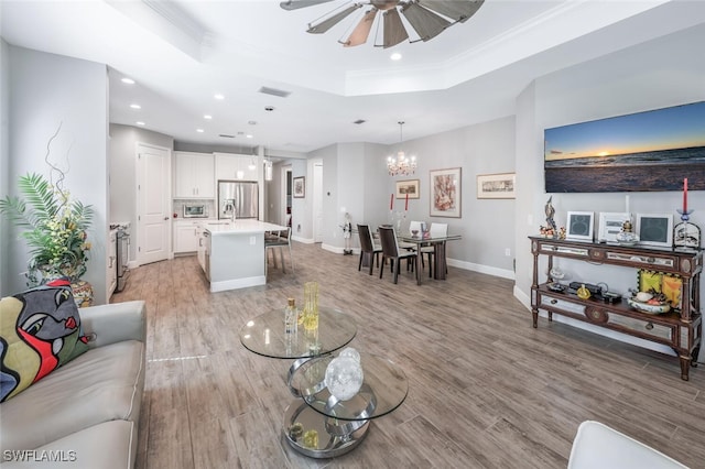 living area with recessed lighting, a tray ceiling, light wood-style floors, and ceiling fan with notable chandelier