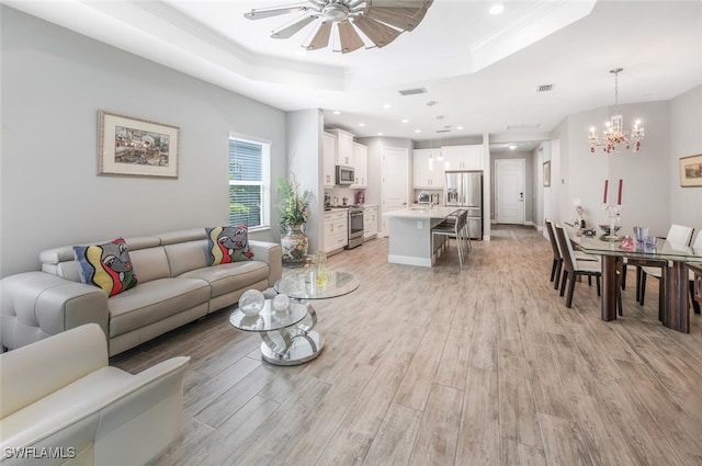 living area featuring visible vents, light wood-type flooring, ceiling fan with notable chandelier, and a raised ceiling