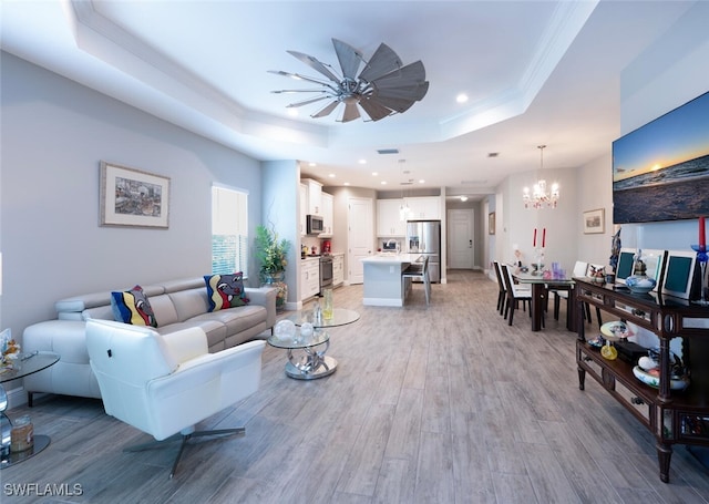 living area with light wood-style floors, ceiling fan with notable chandelier, ornamental molding, recessed lighting, and a raised ceiling