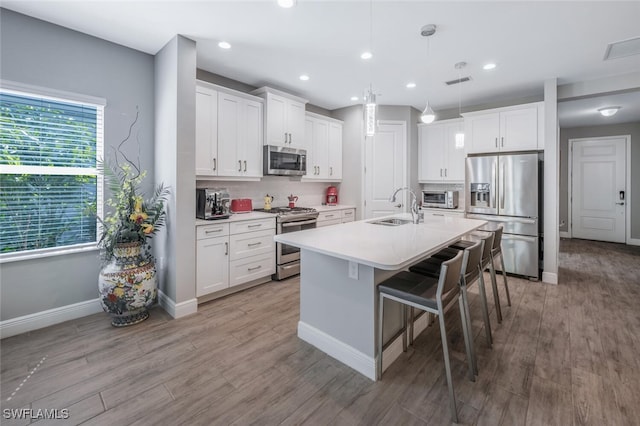 kitchen featuring an island with sink, white cabinetry, a kitchen bar, stainless steel appliances, and a sink