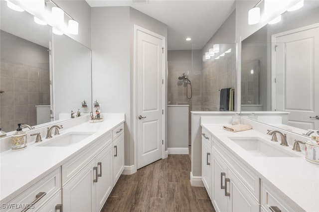 full bath featuring a sink, two vanities, a walk in shower, and wood finished floors