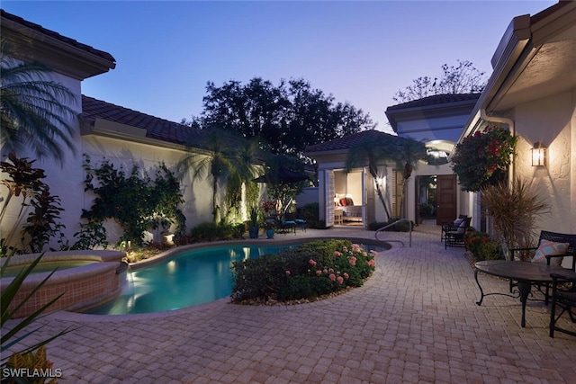 pool at dusk featuring a patio and a pool with connected hot tub