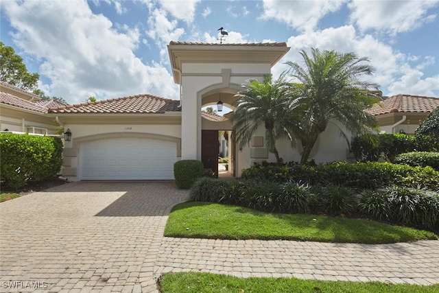 mediterranean / spanish-style home featuring a garage, stucco siding, a tiled roof, and decorative driveway