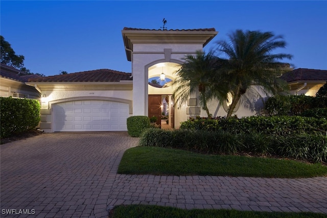 mediterranean / spanish home featuring a tiled roof, a garage, decorative driveway, and stucco siding