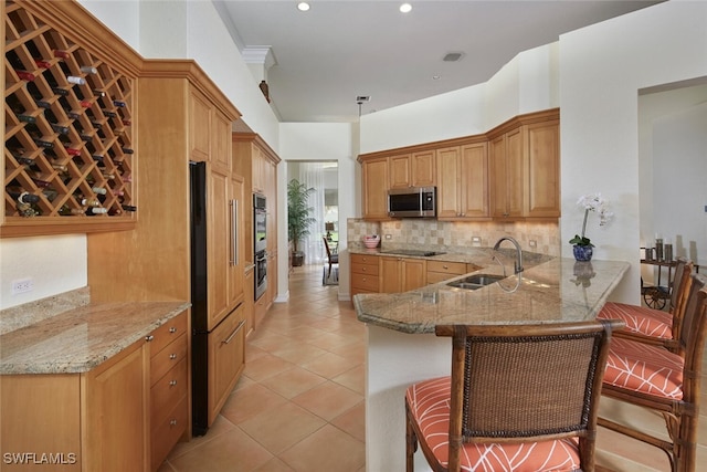 kitchen with stainless steel microwave, backsplash, light stone countertops, black electric cooktop, and a sink