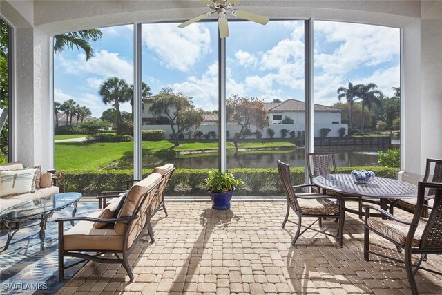 sunroom featuring a water view, brick floor, a ceiling fan, and outdoor dining area