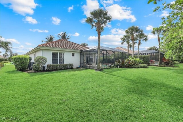 16017 Delarosa Ln, Naples, FL 34110 - rear view of house with glass enclosure, a yard, a tiled roof, and stucco siding