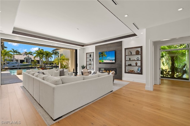 living room featuring light wood-type flooring, built in shelves, a large fireplace, a raised ceiling, and visible vents