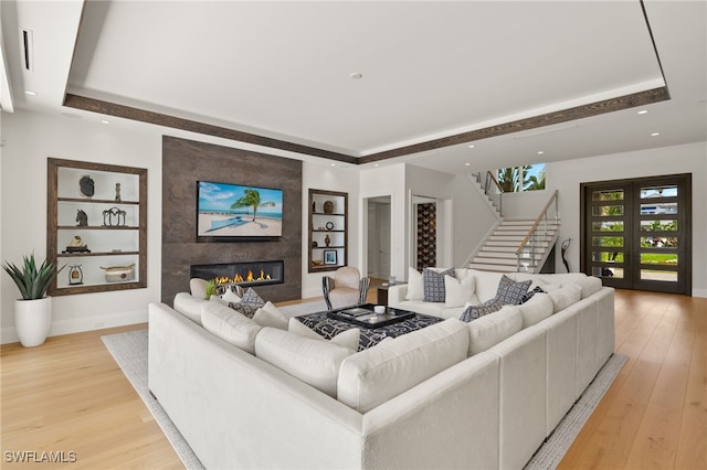 living room featuring stairway, built in features, a large fireplace, and light wood-type flooring
