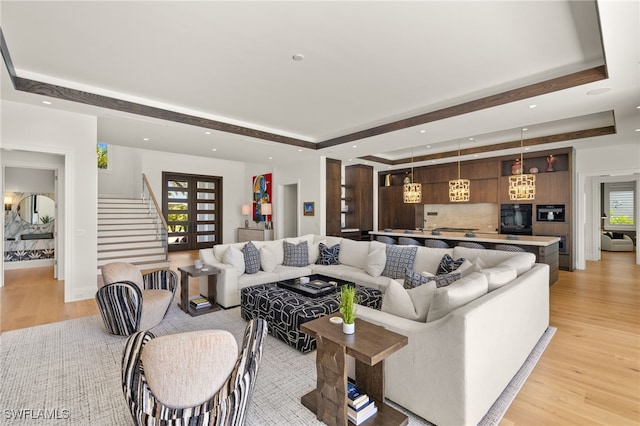 living room with a tray ceiling, light wood-type flooring, stairs, and plenty of natural light