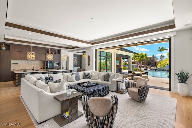 living area with recessed lighting, an inviting chandelier, a tray ceiling, and light wood-style floors