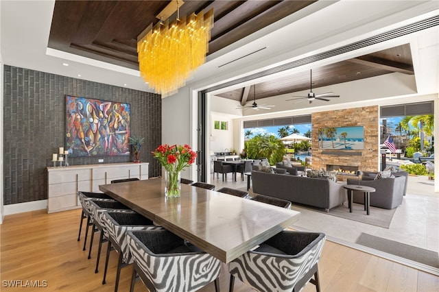 dining space with ceiling fan, an accent wall, wood finished floors, and a raised ceiling