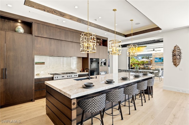 kitchen with light wood finished floors, a large island, a sink, a kitchen bar, and tasteful backsplash