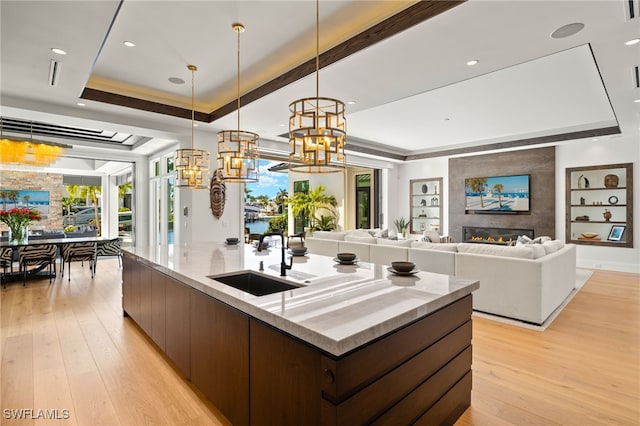 kitchen featuring a sink, a chandelier, a kitchen island with sink, light wood-type flooring, and a tray ceiling