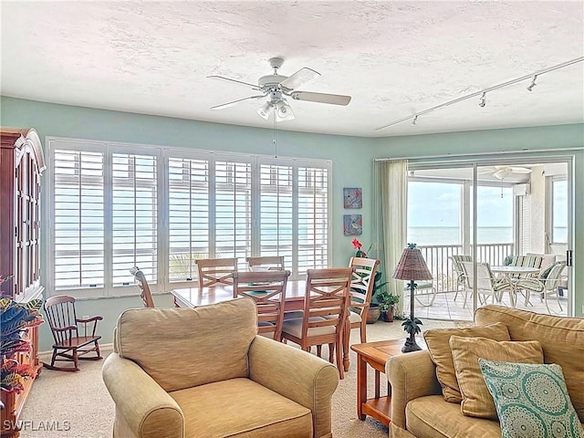 carpeted living area with a textured ceiling, ceiling fan, baseboards, and a healthy amount of sunlight
