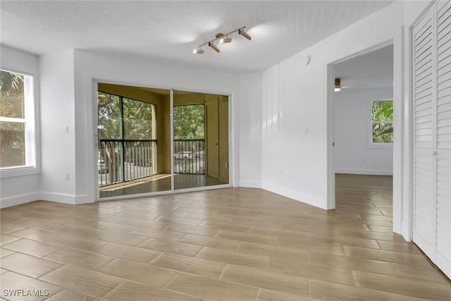 empty room with rail lighting, baseboards, and a textured ceiling