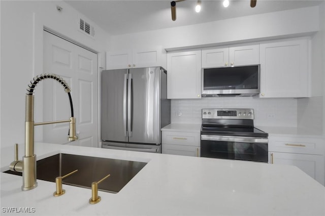 kitchen featuring white cabinets, appliances with stainless steel finishes, light countertops, a sink, and backsplash