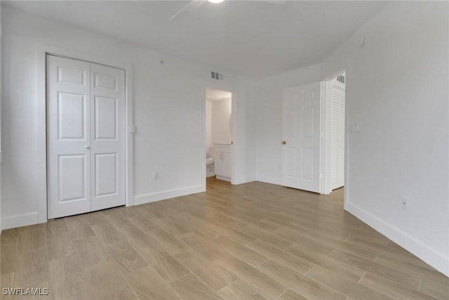 unfurnished bedroom featuring light wood-type flooring, ensuite bathroom, baseboards, and visible vents