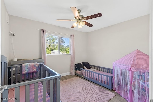 bedroom featuring baseboards, wood finished floors, a crib, and a ceiling fan