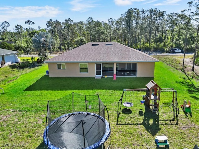 rear view of property with stucco siding, a trampoline, a lawn, and a playground
