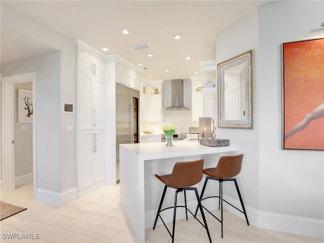 365 5th Ave S Unit 307, Naples, FL 34102 - kitchen with wall chimney exhaust hood, a kitchen bar, a peninsula, white cabinets, and recessed lighting