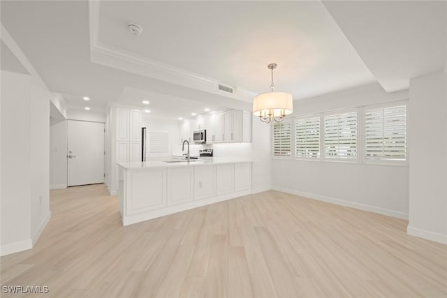 kitchen with a sink, stainless steel microwave, a peninsula, a chandelier, and white cabinets