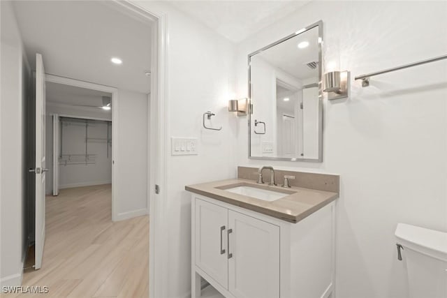 half bathroom with baseboards, wood finished floors, vanity, toilet, and recessed lighting