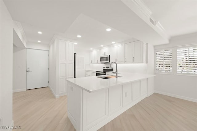 kitchen featuring a sink, appliances with stainless steel finishes, light wood-style flooring, baseboards, and crown molding