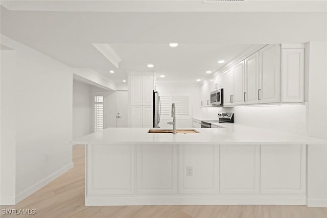 kitchen featuring appliances with stainless steel finishes, a sink, a peninsula, light countertops, and recessed lighting