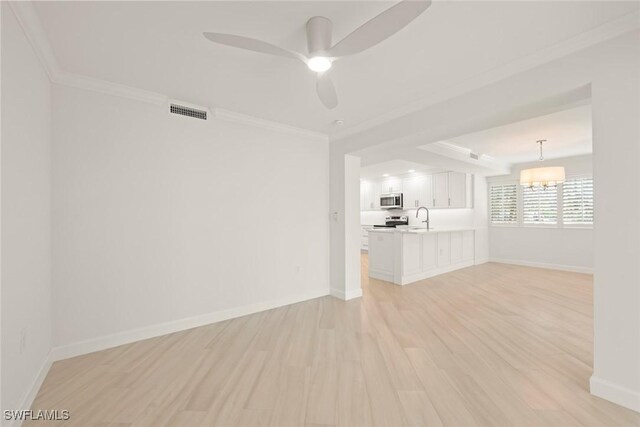 unfurnished living room featuring light wood-style floors, a sink, ornamental molding, baseboards, and ceiling fan