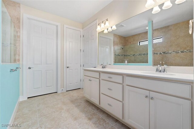 bathroom featuring double vanity, a tile shower, tile patterned flooring, and a sink
