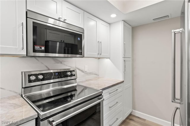 kitchen with white cabinetry, light wood-style flooring, stainless steel appliances, baseboards, and visible vents