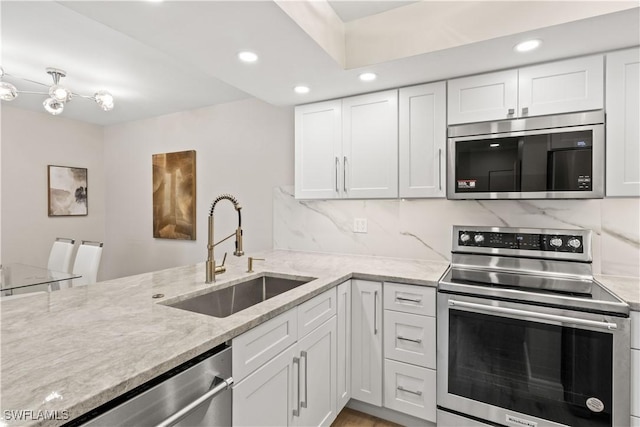 kitchen featuring white cabinets, stainless steel appliances, a sink, light stone counters, and backsplash