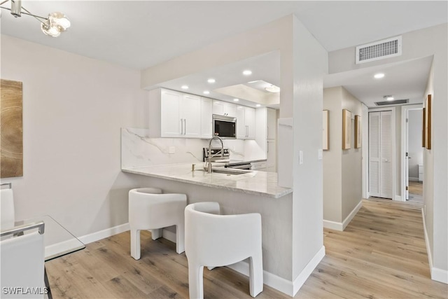 kitchen featuring backsplash, a sink, light wood finished floors, visible vents, and appliances with stainless steel finishes