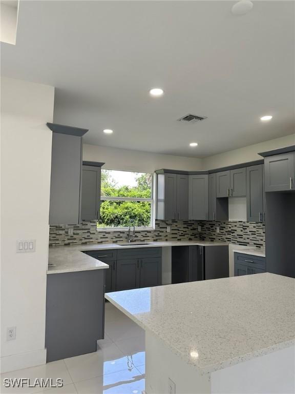 718 Chattman St E, Lehigh Acres, FL 33974 - kitchen featuring a sink, gray cabinetry, decorative backsplash, light stone countertops, and a center island