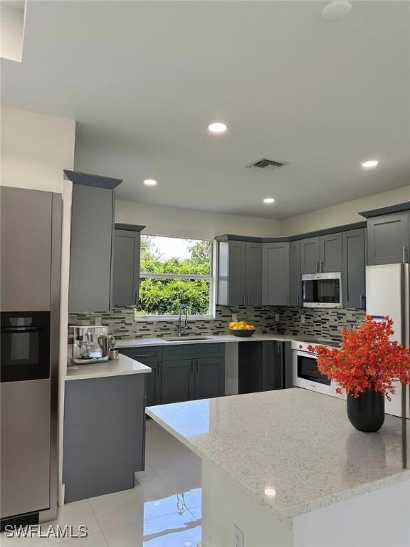 718 Chattman St E, Lehigh Acres, FL 33974 - kitchen featuring appliances with stainless steel finishes, a sink, tasteful backsplash, gray cabinets, and light stone counters