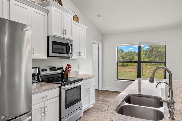 490 Windermere Dr, Lehigh Acres, FL 33972 - kitchen featuring white cabinetry, vaulted ceiling, stainless steel appliances, a sink, and light wood-style flooring