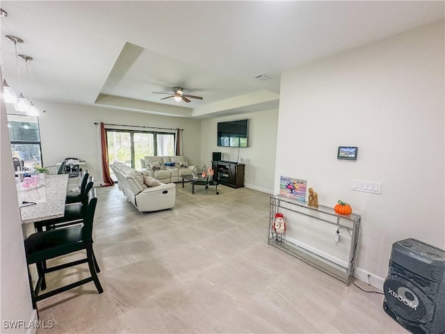 living room featuring a ceiling fan, baseboards, visible vents, and a raised ceiling