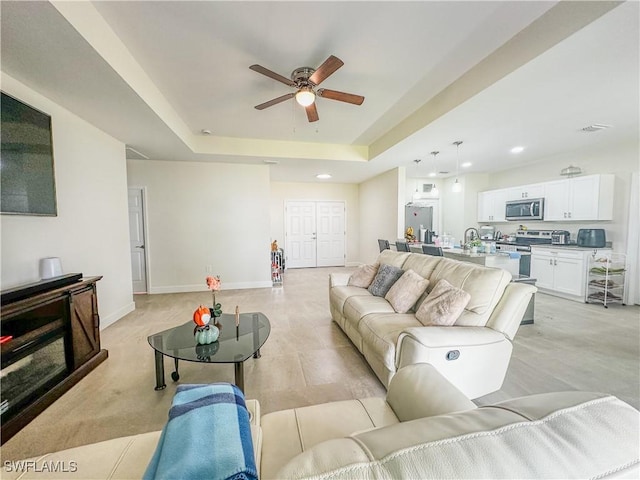 living area with recessed lighting, a ceiling fan, a raised ceiling, and baseboards