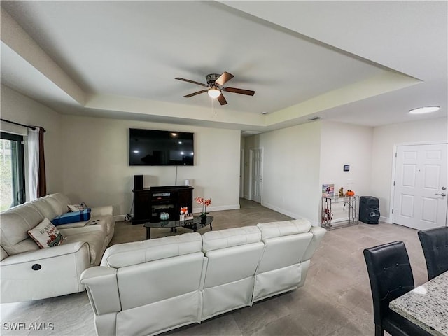 living area featuring baseboards, a ceiling fan, and a tray ceiling