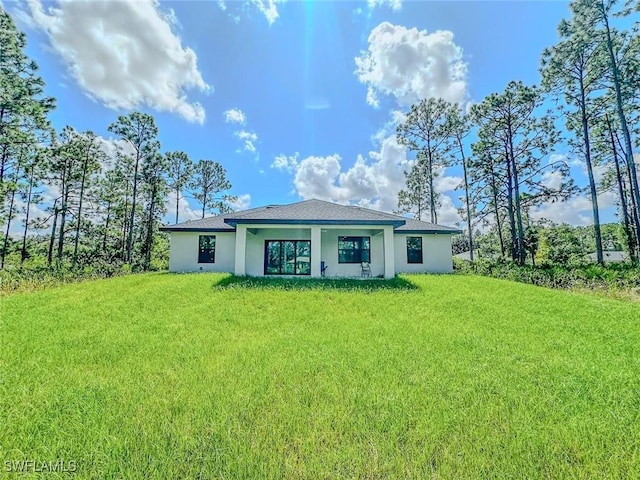 back of house with a lawn, stucco siding, and roof with shingles