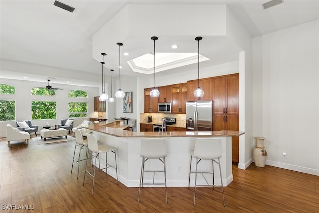 27549 Riverbank Dr, Bonita Springs, FL 34134 - kitchen featuring visible vents, a kitchen breakfast bar, brown cabinets, wood finished floors, and stainless steel appliances