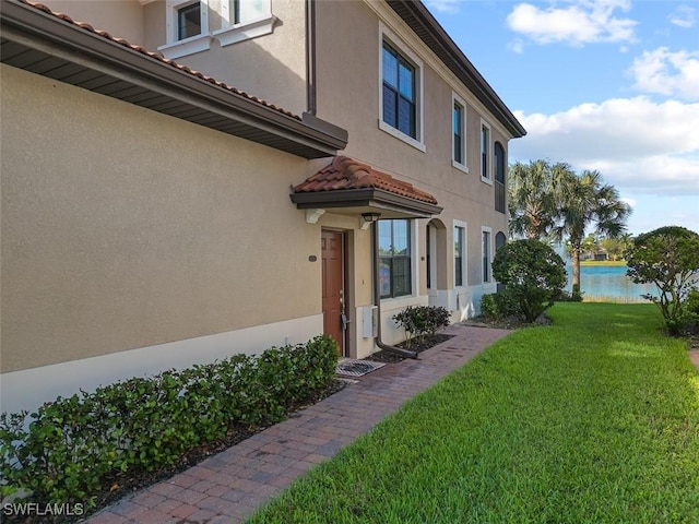 view of property exterior with a tiled roof, a water view, stucco siding, and a yard