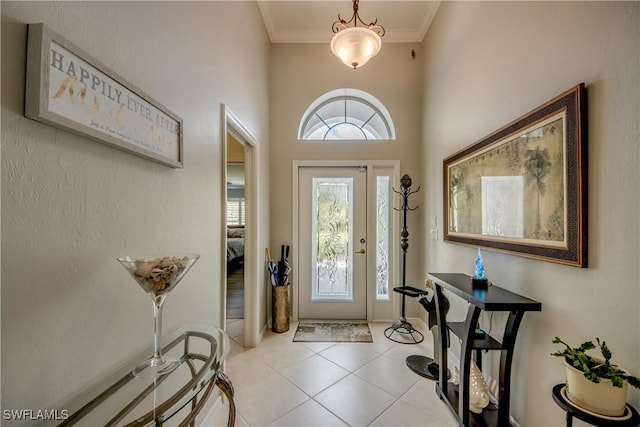 entryway with a towering ceiling, light tile patterned floors, and crown molding