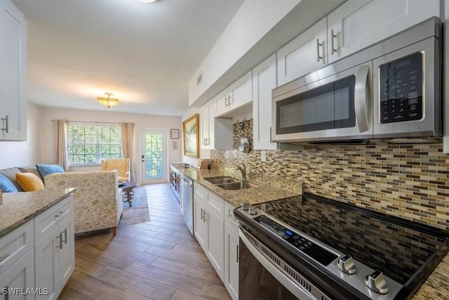 kitchen with a sink, stainless steel appliances, white cabinetry, light wood-type flooring, and tasteful backsplash