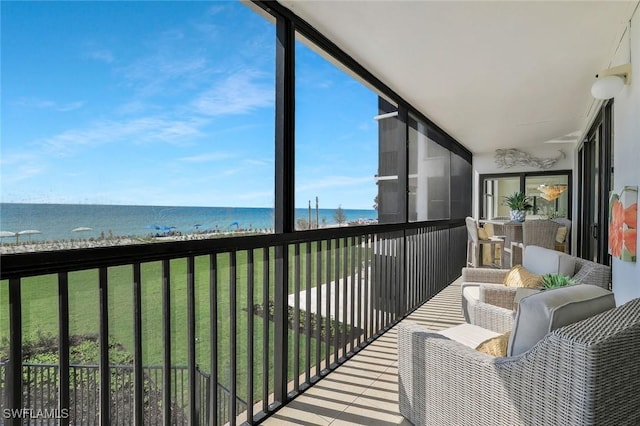 sunroom featuring expansive windows, a water view, and a view of the beach