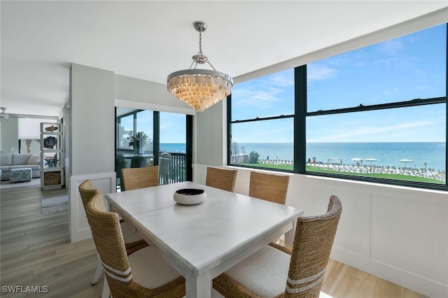 dining space with a water view, a decorative wall, a chandelier, and light wood-type flooring