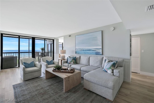 living room featuring baseboards, expansive windows, visible vents, and light wood-style floors