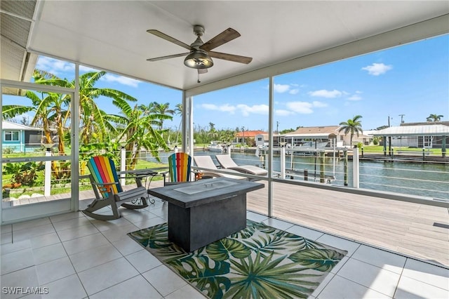 sunroom with a wall of windows, a water view, tile patterned flooring, and a ceiling fan